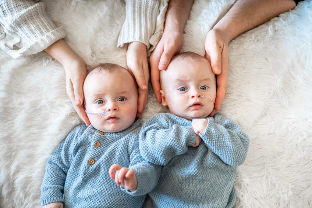 twin newborn boys with their parents hands