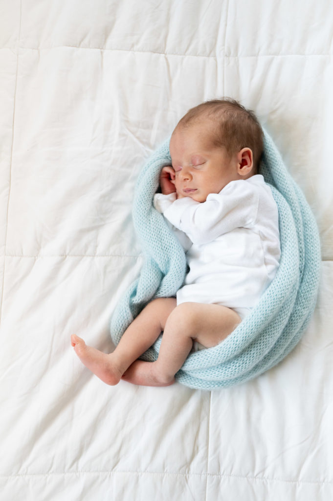baby boy wrapped in blue knit blanket sleeping on bed with a white blanket