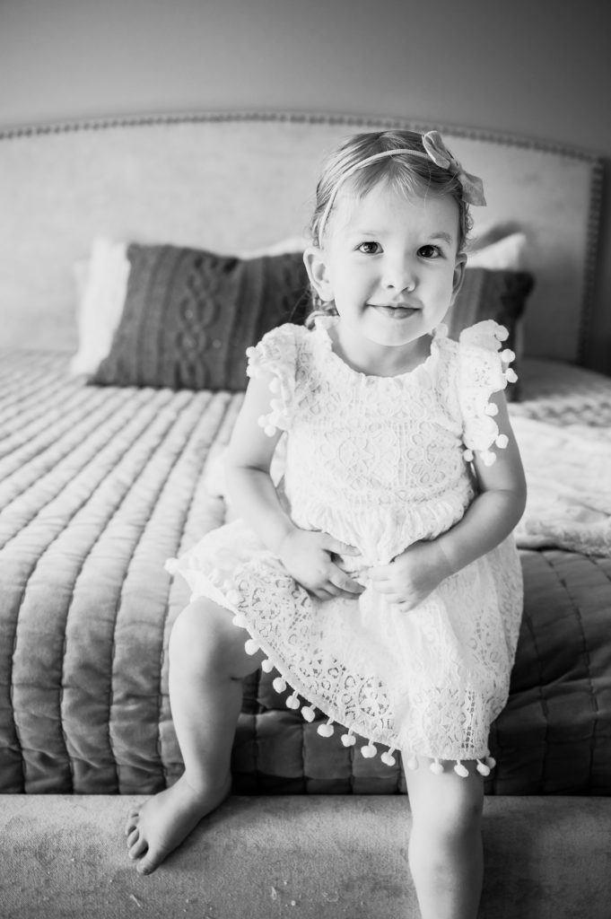 black and white picture of toddler sitting on the end of a bed