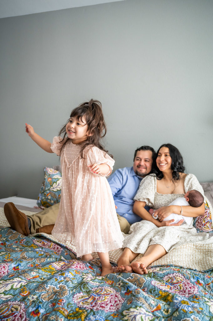 Toddler jumps on bed while family watches during newborn photography