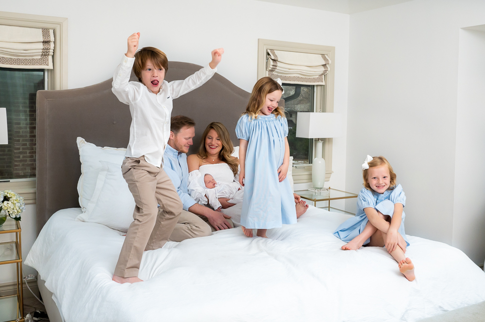 3 older siblings jump on bed during newborn photos