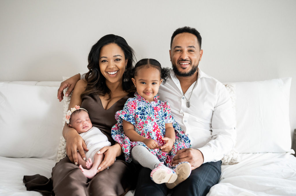 Family with toddler and newborn smiling for the camera
