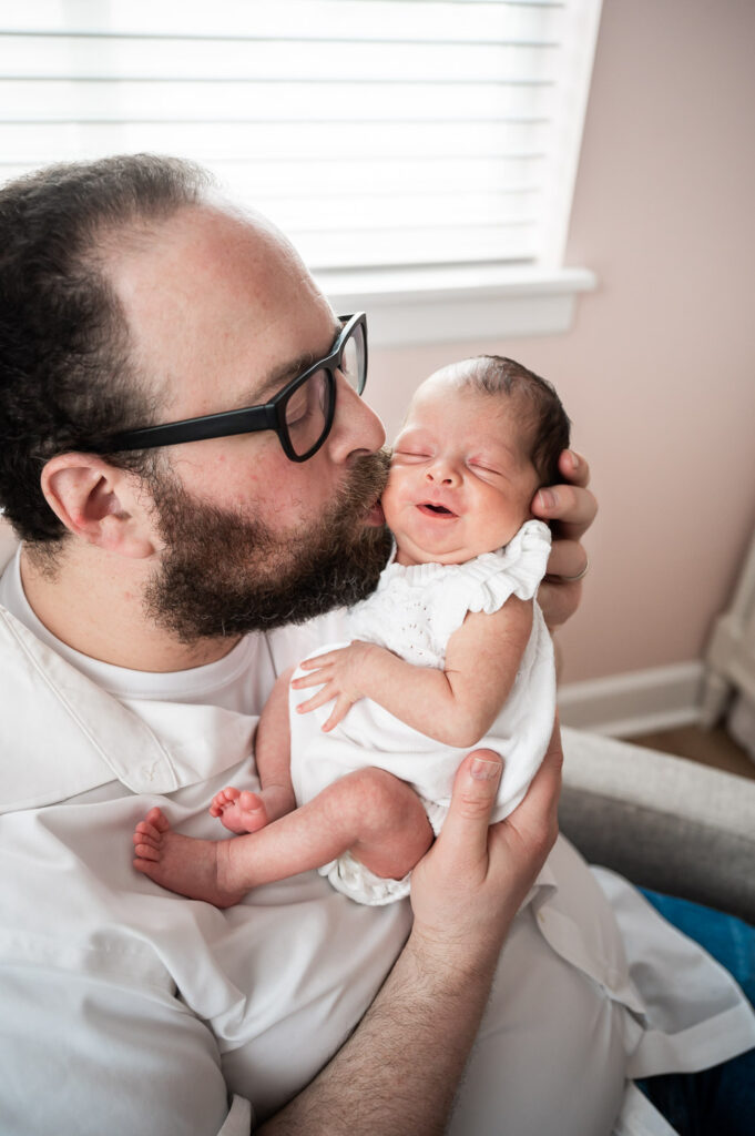 baby smiling while Dad with beard kisses her cheek