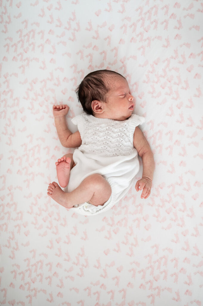baby laying naturally on pick crib sheet with one foot pointing up toward the camera