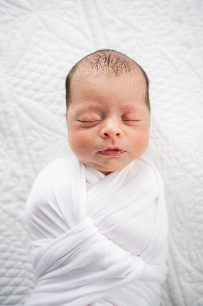 baby swaddled in white wrap sleeping on white blanket