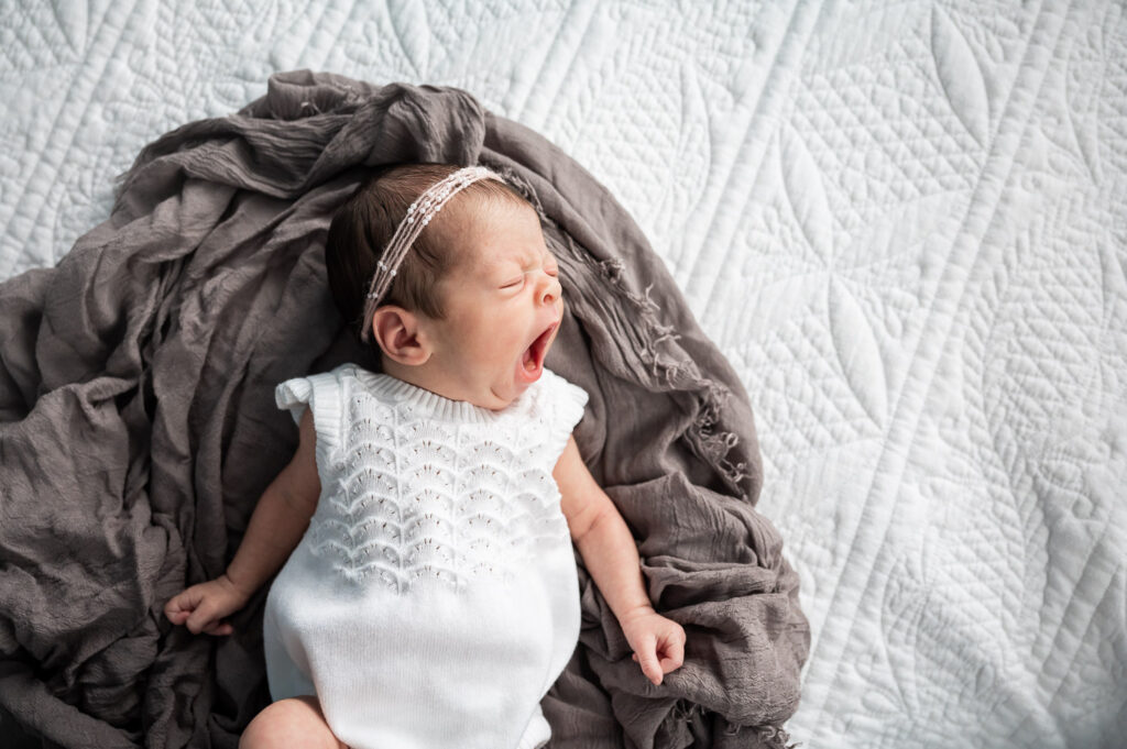 baby yawning on deep purple fabric in a circle shape on a white blanket